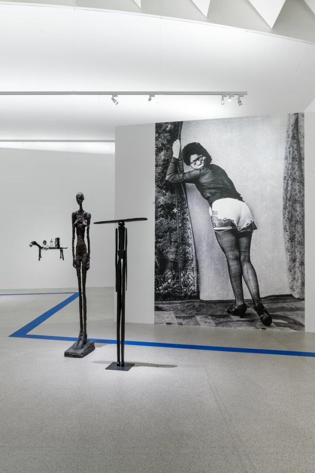 In einer Galerie stehen Skulpturen und ein großes Schwarz-Weiß-Foto einer Frau.