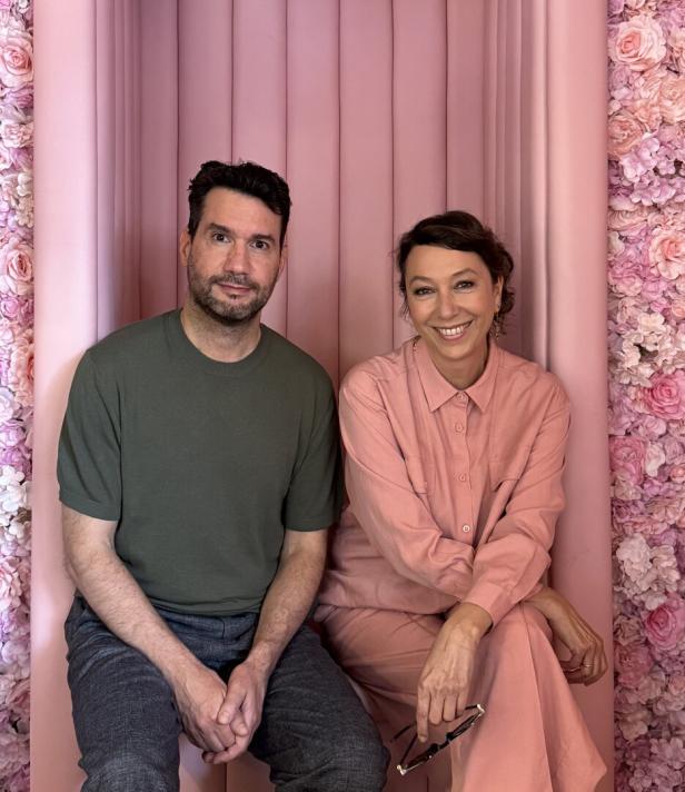 Ein Mann und eine Frau sitzen vor einem rosa Hintergrund mit Blumen.