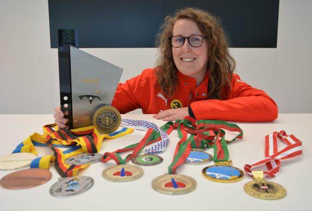 Eine Frau mit Brille präsentiert stolz ihre Minigolf-Trophäen und Medaillen.