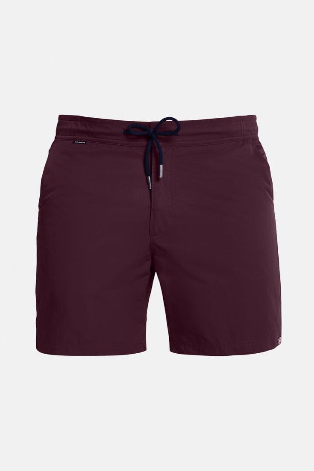 Eine weinrote Badeshorts mit marineblauer Kordel vor einem weißen Hintergrund.