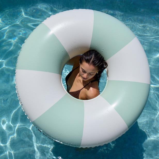 Eine Frau entspannt in einem mintgrün-weiß gestreiften Schwimmreifen im Pool.