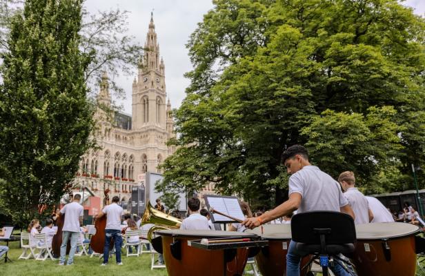 Eine Gruppe von Menschen spielt Trommeln in einem Park, umgeben von Bäumen und Wiese.