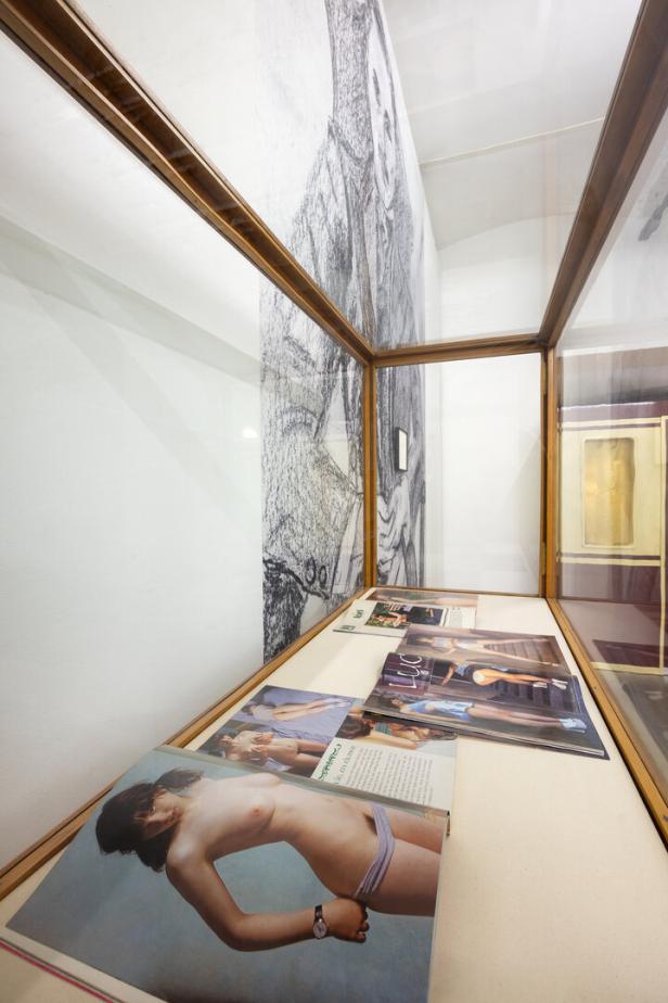 Eine Vitrine zeigt Zeitschriften mit Aktfotografien und eine Bleistiftzeichnung an der Wand.