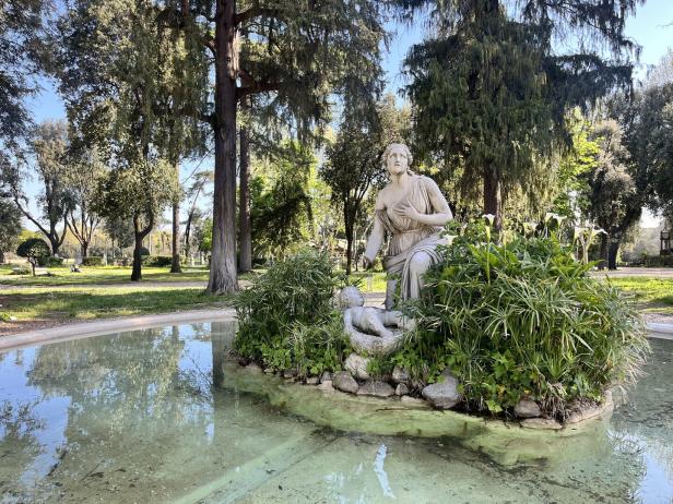Eine Statue einer Frau mit Kind in einem Brunnen in einem Park.