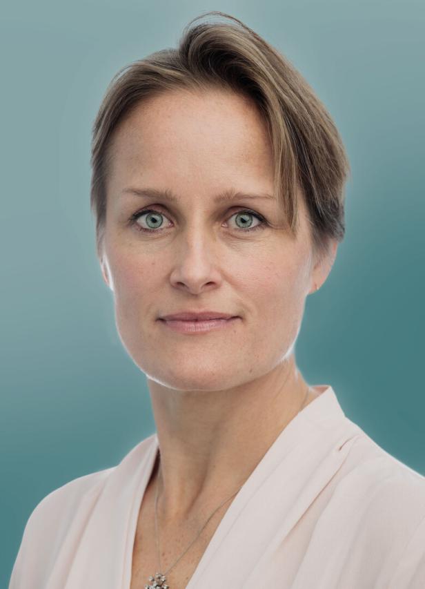 Porträt einer Frau mit kurzem, blondem Haar und einem hellen Oberteil vor blauem Hintergrund.