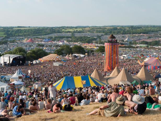 Blick über das Glastonbury Festival mit Menschenmassen, Bühnen und Zelten.