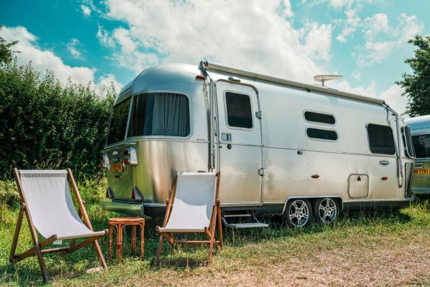 Ein silberner Airstream-Wohnwagen steht auf einer Wiese mit zwei Liegestühlen davor.