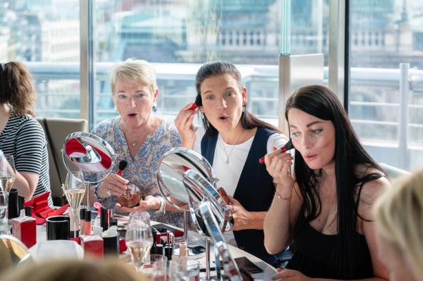 Frauen bei einem Beauty-Workshop sitzen an einem Tisch und verwenden Make-up-Pinsel für ihre Anwendungen.