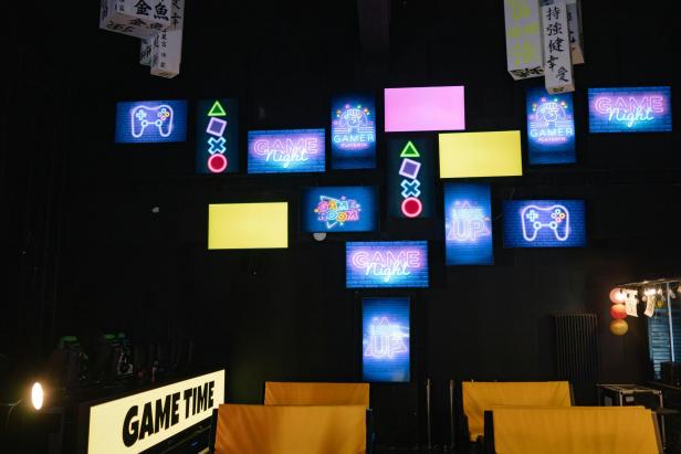 Ein Raum voller Videospielkonsolen, beleuchtet von einer Wand mit bunten Neonlichtern.