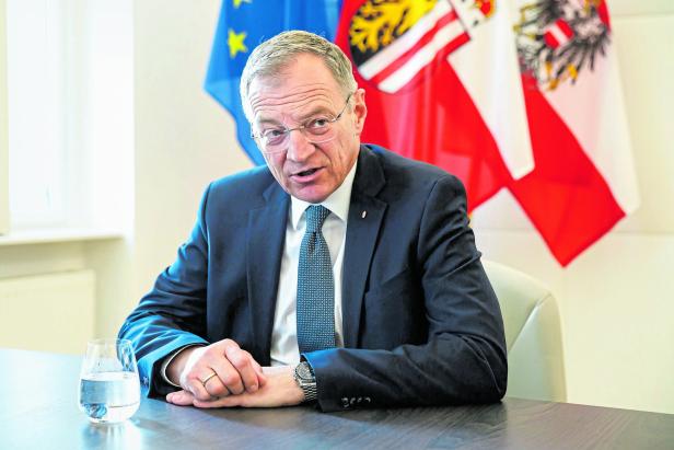 Landeshauptmann Thomas Stelzer sitzt vor der Europa- und Österreichflagge.