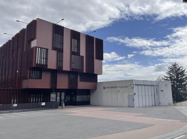 Die Justizanstalt Eisenstadt, ein modernes Gebäude mit brauner Fassade, unter blauem Himmel.