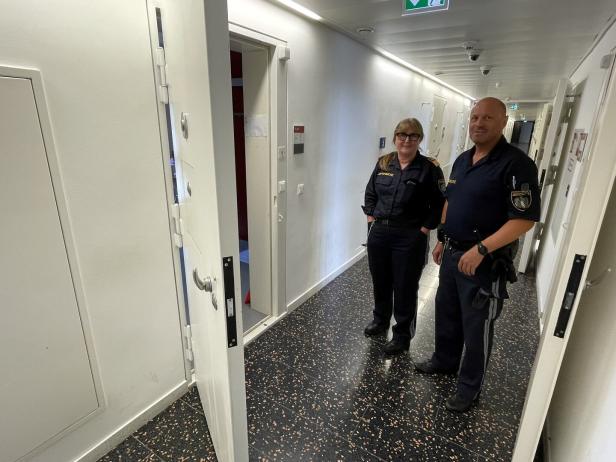 Zwei Justizvollzugsbeamte stehen in einem Flur mit Zellentüren.