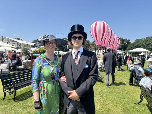 Eine Frau mit Hut und ein Mann mit Zylinder posieren auf dem Royal Ascot-Gelände.