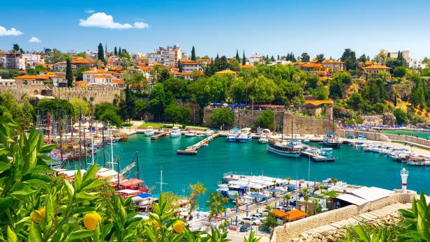 Ein Hafen mit zahlreichen Booten liegt vor der Stadt Antalya mit roten Dächern und viel Grün.