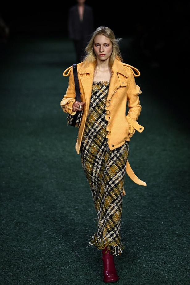 Ein Model auf dem Laufsteg bei einer Burberry-Modenschau in einem gelben Mantel und einem karierten Hosenanzug.