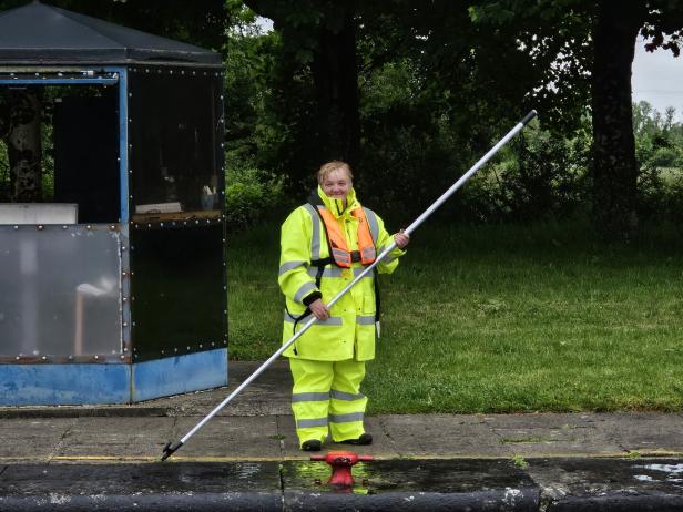 Eine Frau in Arbeitskleidung reinigt mit einem langen Stab eine Wasserfläche.