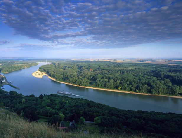 Ein Fluss schlängelt sich durch eine grüne Landschaft unter einem bewölkten Himmel.