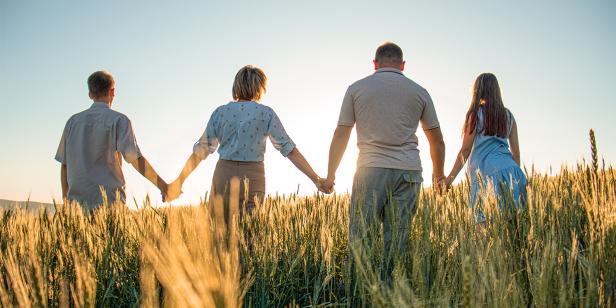 Eine Gruppe von Menschen hält sich in einem Feld an den Händen und steht in einer harmonischen Pose zusammen.