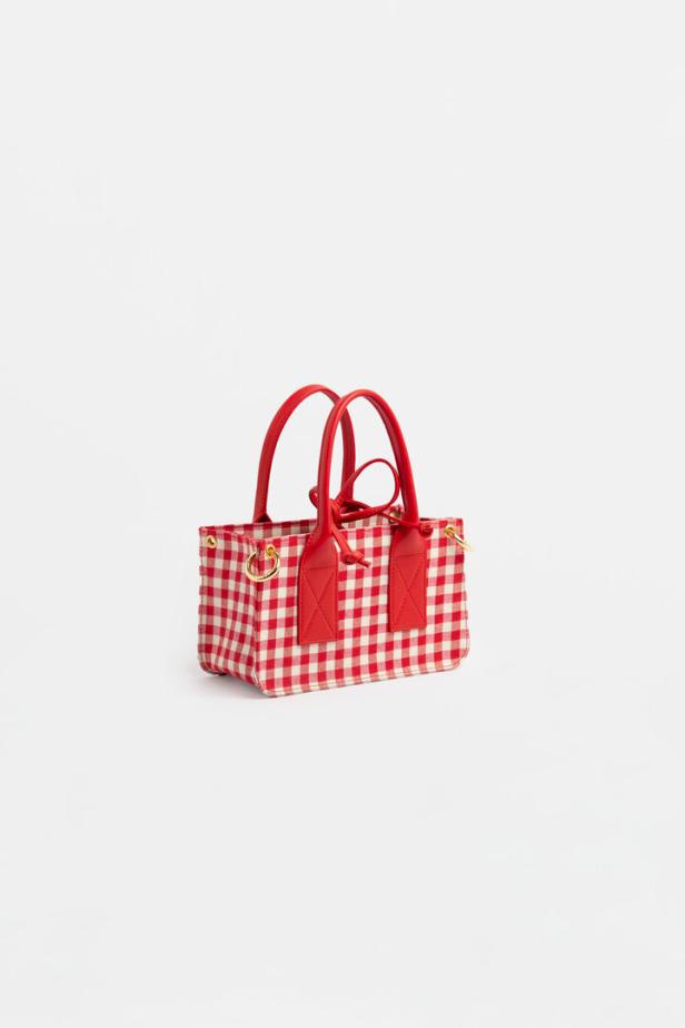 Eine kleine Handtasche mit rotem Karomuster und roten Henkeln vor einem weißen Hintergrund.