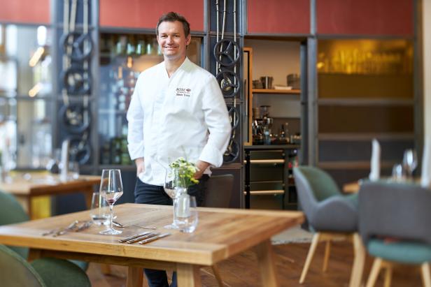 Koch Simon Tress posiert in seinem Restaurant Rose vor einem gedeckten Holztisch.
