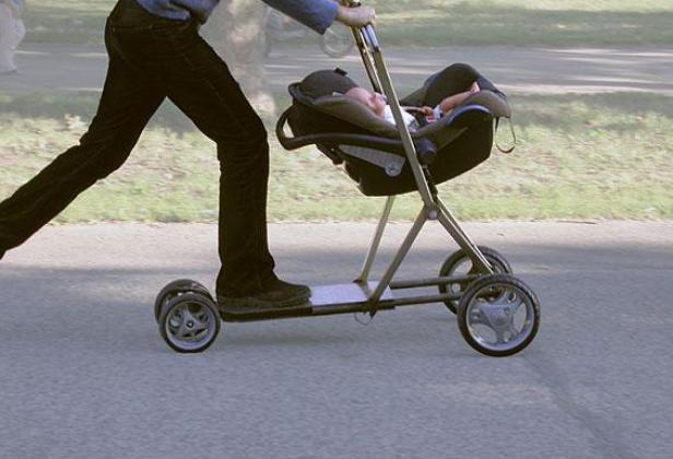 Eine Person schiebt einen Kinderwagen, der auf einer Art Roller montiert ist, auf einer Straße.