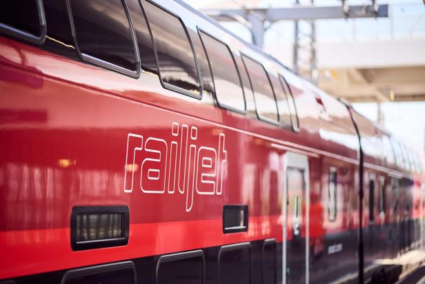 Ein roter Railjet-Zug steht an einem Bahnhof.