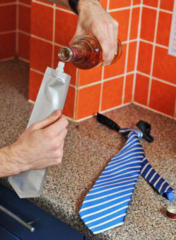 Eine Person füllt eine Flasche Alkohol in einen silbernen Beutel, während eine Krawatte auf der Theke liegt.