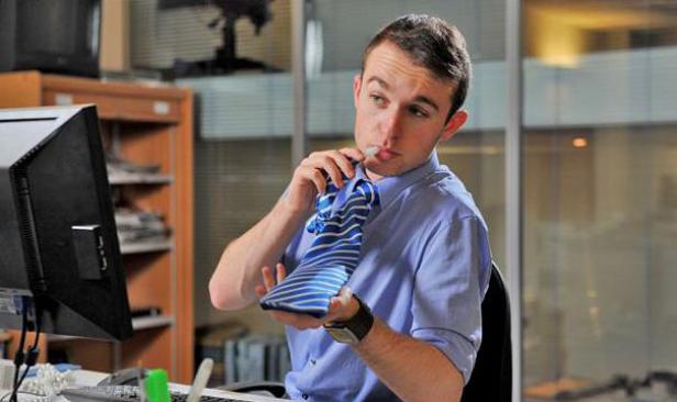 Ein Mann im Büro hält eine Krawatte und hat einen Stift im Mund.