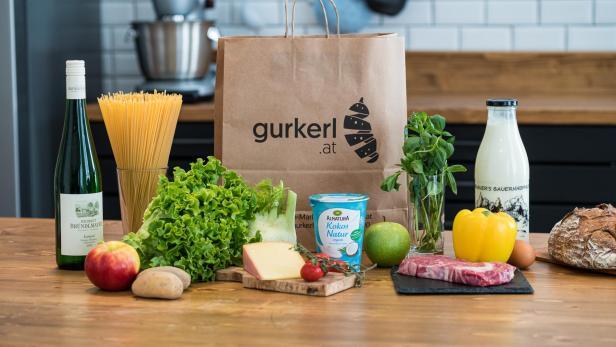 Eine Einkaufstüte von gurkerl steht auf einer Anrichte. Darum stehen frische Lebensmittel. 