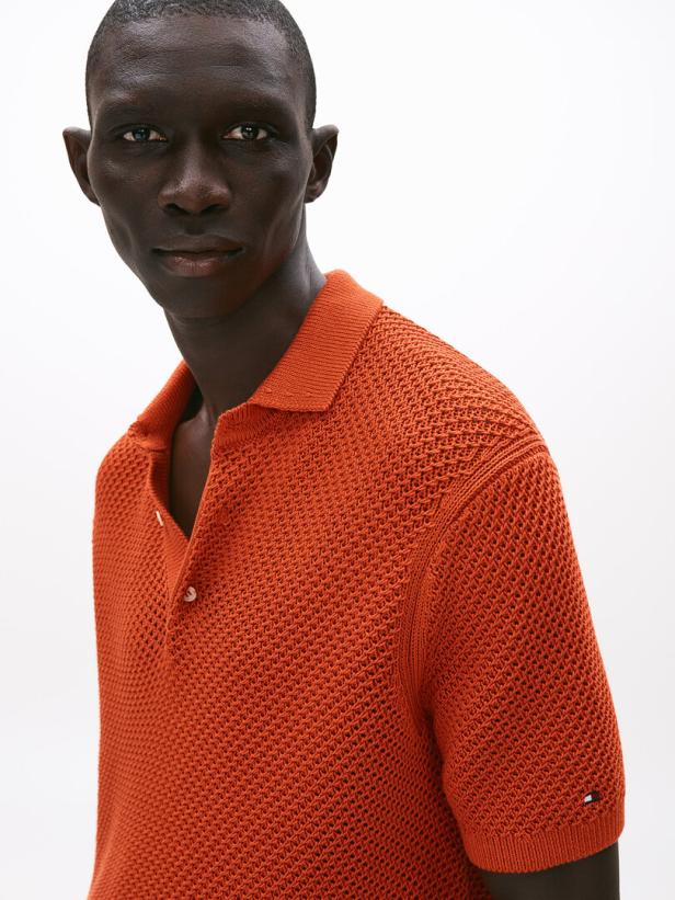 Ein Mann mit dunkler Haut trägt ein orangefarbenes Strickpolohemd.