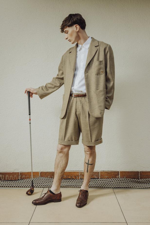 Ein Mann im karierten Anzug mit Golfschläger posiert vor einer Wand.