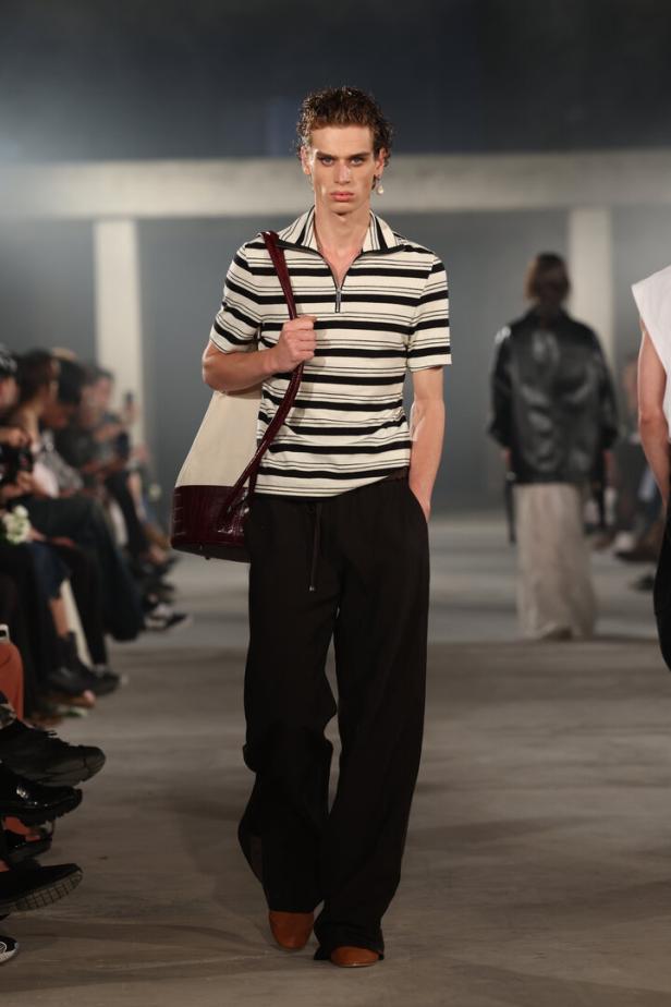 Ein Mann mit gestreiftem Hemd und Tasche läuft auf einem Laufsteg während der Pariser Fashion Week.