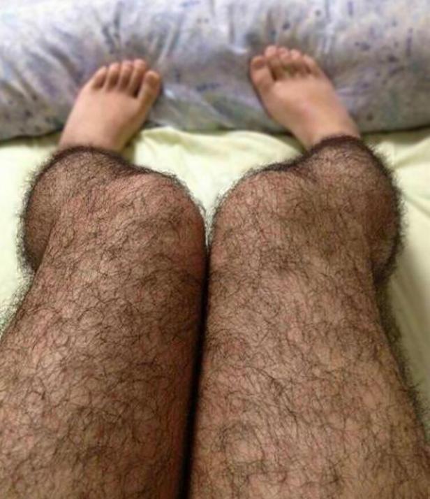 Behaarte Beine und Füße liegen auf einem Bett.