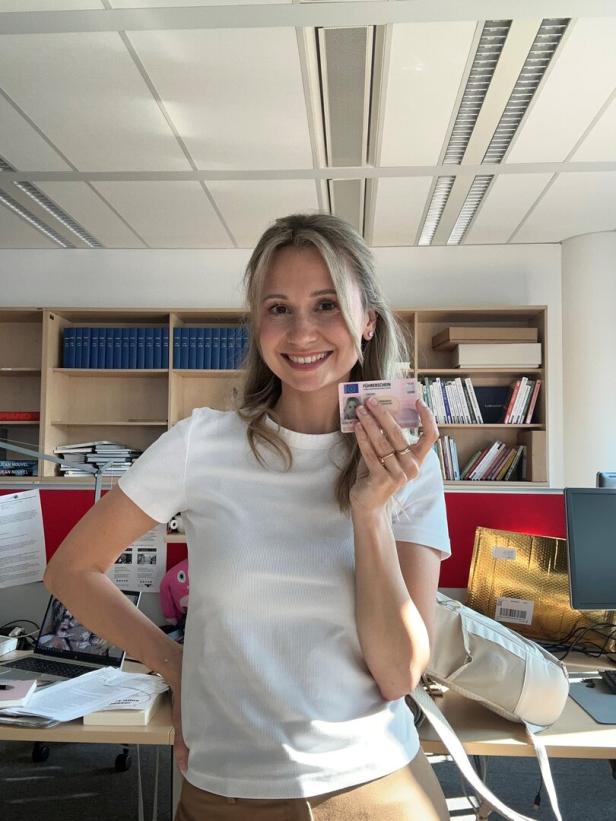 Eine Frau hält lächelnd ihren neuen Führerschein in die Kamera.