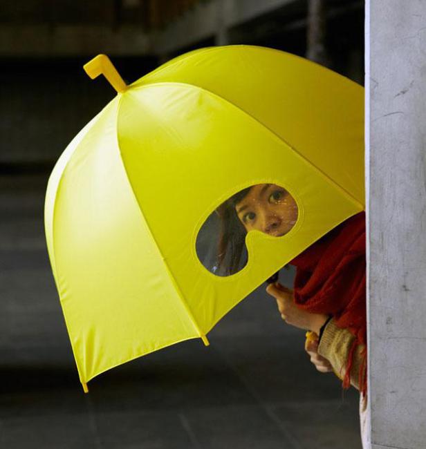 Eine Frau schaut durch ein Sichtfenster in einem gelben Regenschirm.