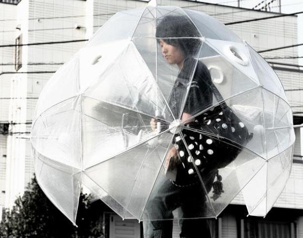 Eine Person geht mit einem großen, transparenten Kuppelschirm die Straße entlang.