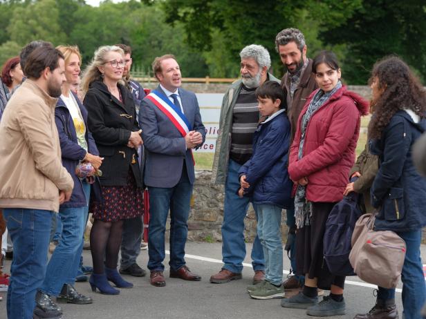 Eine Gruppe von Menschen steht im Freien, darunter ein Mann mit einer Schärpe in den französischen Nationalfarben.