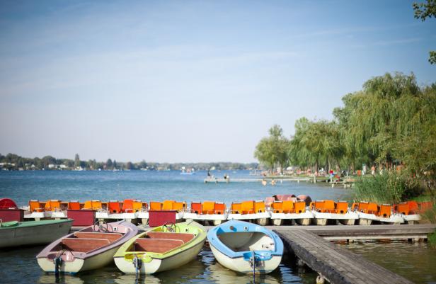 Mehrere bunte Boote liegen an einem Steg an einem See.