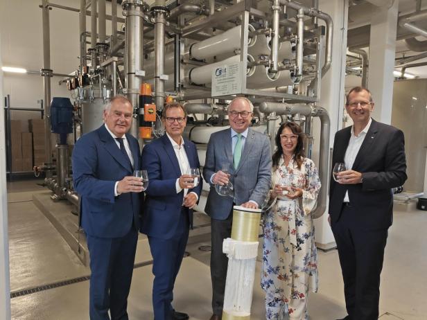 Fünf Personen stehen vor einer Wasseraufbereitungsanlage und halten Gläser mit Wasser.