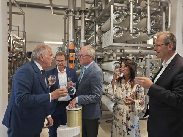 Eine Gruppe von Personen steht vor einer Wasseraufbereitungsanlage und trinkt Wasser.