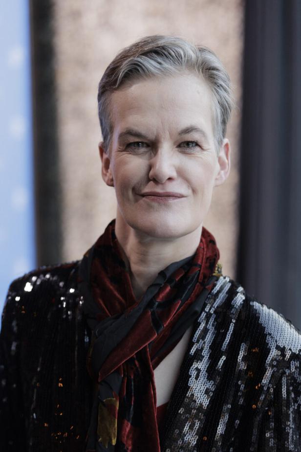 Nahaufnahme einer Frau mit kurzem, grauem Haar, die eine paillettenbesetzte Jacke und einen Schal trägt.