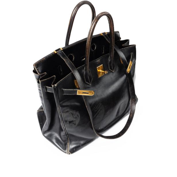 Eine schwarze Lederhandtasche mit goldenen Akzenten steht auf einem weißen Hintergrund.