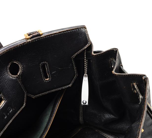Detailansicht einer geöffneten, schwarzen Lederhandtasche mit silbernem Anhänger.