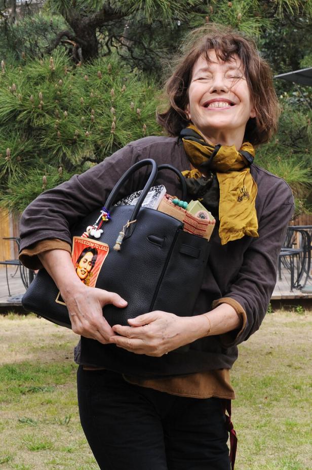 Jane Birkin lächelt und hält eine Handtasche mit einem Bild von Aung San Suu Kyi.