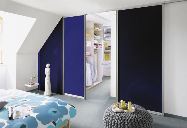 Ein Schlafzimmer mit einem offenen Kleiderschrank hinter blauen Schiebetüren.