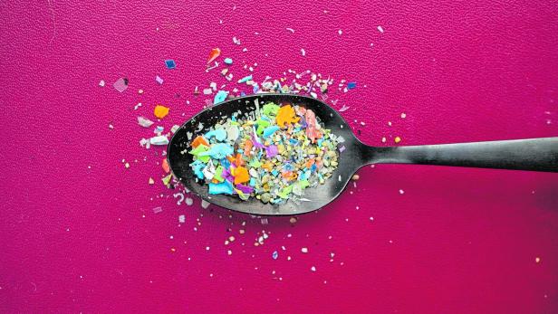 A pile of microplastics gathered from the beach in a spoon against a dark red background.