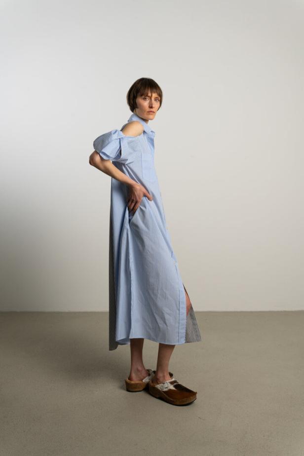 Eine Frau posiert in einem blau-weiß gestreiften Hemdkleid und Clogs.