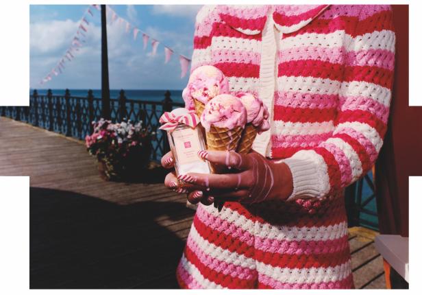 Eine Person im rosa-weiß gestreiften Outfit hält Eiswaffeln und eine Flasche Jo Malone „Raspberry Ripple Cologne“.