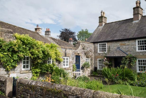 Ein malerisches Steinhaus mit einem blauen Türrahmen und üppigem Grün im Garten.