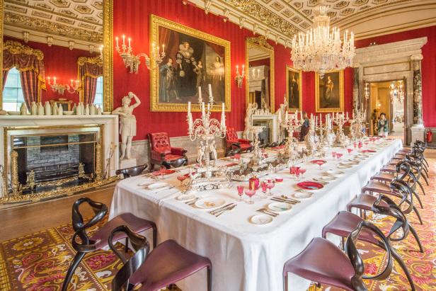 Ein reich gedeckter Esstisch in einem opulenten Speisesaal mit roter Wandbespannung.